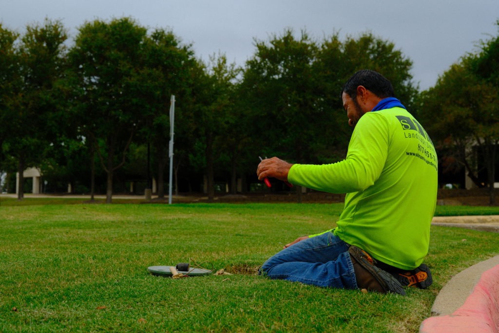 Irrigation crew member connecting sprinkler system wires during repair at commercial property
