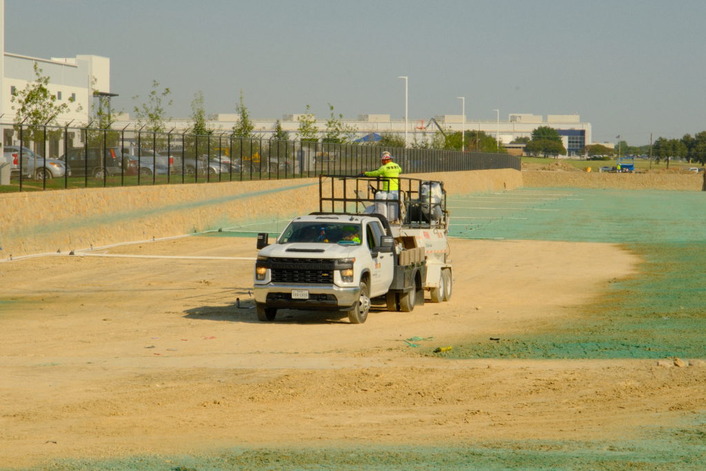 Hydromulch being sprayed over soil at large commercial parking lot construction site.