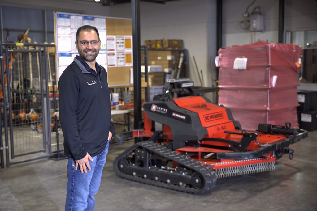 SLD's Maintenance Operations Manager standing next to a remote-controlled mower in Lewisville.