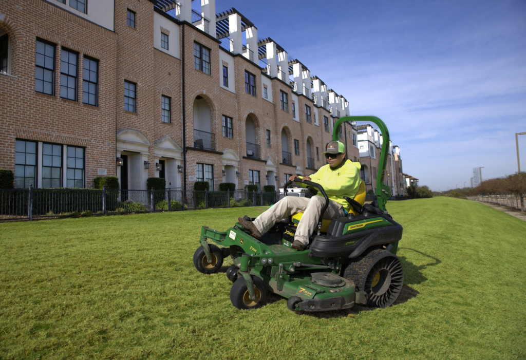 SLD crew member mowing turf with a John Deere mower at an HOA property in the DFW area.