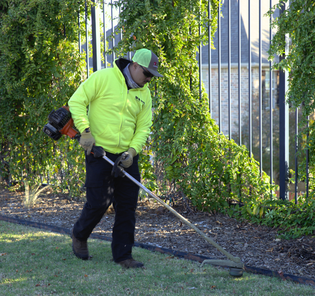 SLD crew member trimming edges with a weed eater at a commercial property in the DFW area.
