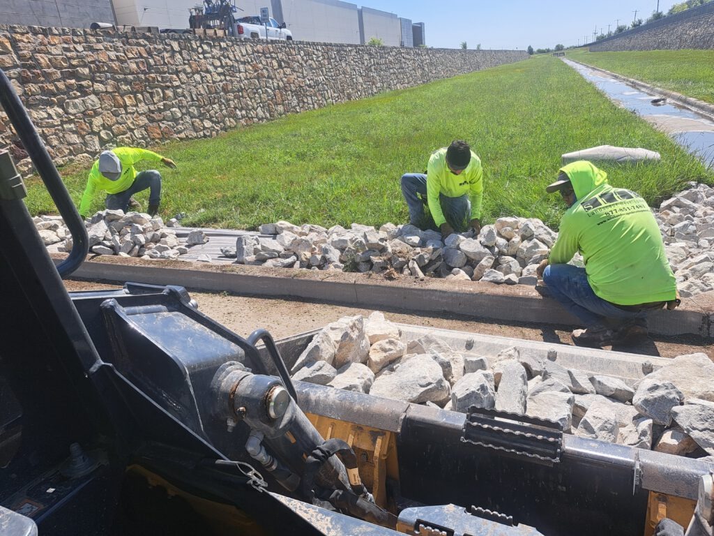 SLD crew members setting rock by hand along a drainage area next to a retaining wall at a commercial property in DFW.