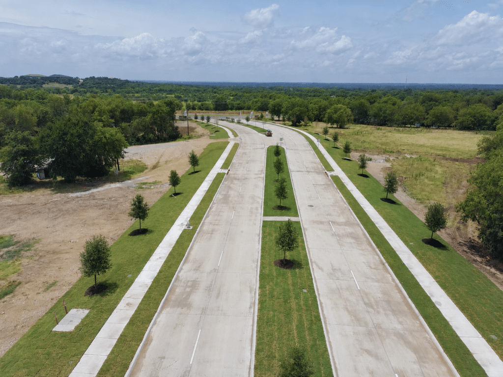 Aerial view of a new divided roadway in DFW with fresh sod and newly planted street trees along the parkways and center median, installed by SLD.